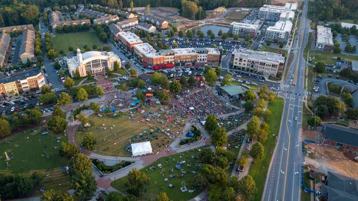 Aerial view of Suwanee Town Center Park filled with people enjoying an outdoor event, surrounded by residential and commercial buildings, highlighting the community atmosphere in Gwinnett County.