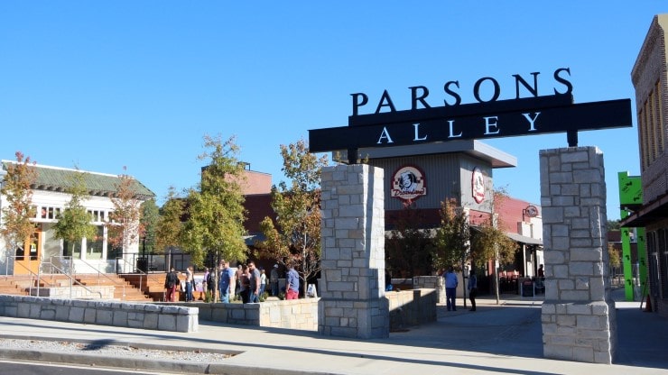Parsons Alley entrance with stone pillars, bustling crowd, and shops in Duluth, GA, highlighting local businesses and community engagement.