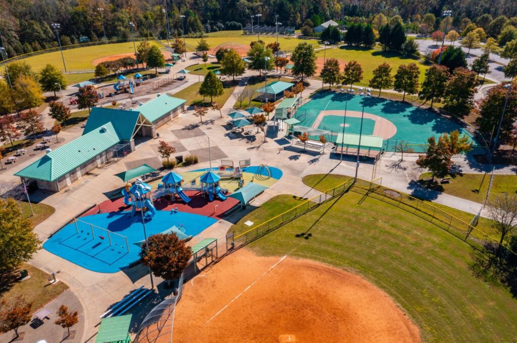Aerial view of Bay Creek Park in Loganville, GA, showcasing playground equipment, baseball field, and picnic areas surrounded by trees, illustrating community recreational space.