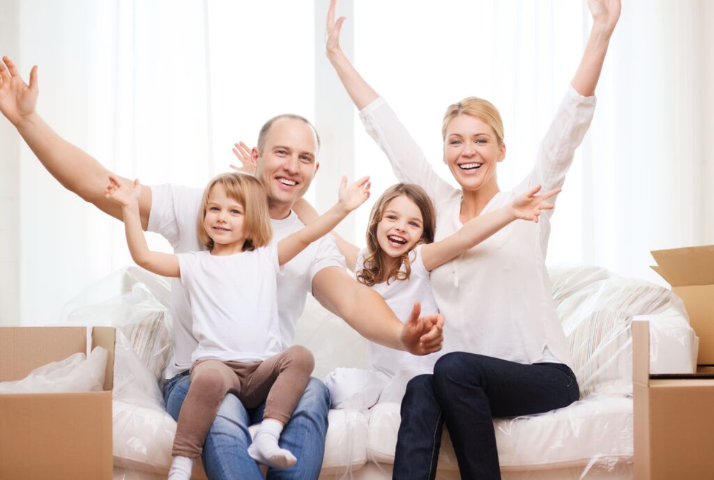 Family of four celebrating together on a couch in a newly moved-in home, surrounded by moving boxes, symbolizing comfort and warmth in a family setting.