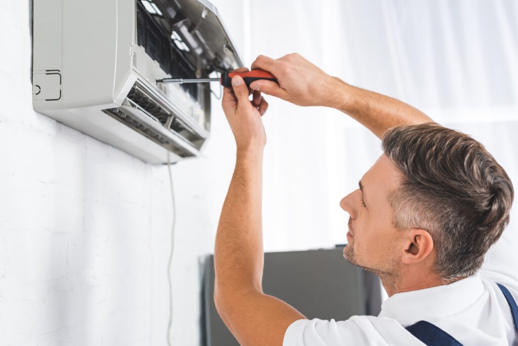 Man repairing an air conditioning unit with a screwdriver, showcasing HVAC expertise in a residential setting.