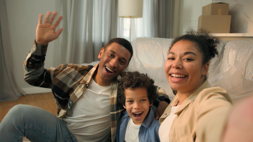 Happy African American family of three smiling and waving in a cozy home setting, representing warmth and comfort, aligning with B Mays Heating & Air&rsquo;s commitment to providing dependable heating services for families in Loganville, GA.